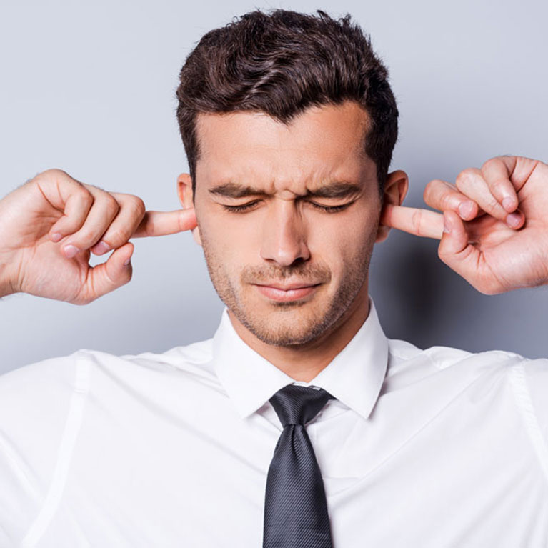 Ein Mann der sich die Finger in die Ohren steckt, damit er nichts mehr hört. Es geht um Tinnitus.