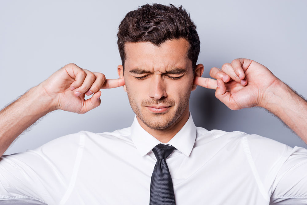 Ein Mann der sich die Finger in die Ohren steckt, damit er nichts mehr hört. Es geht um Tinnitus.